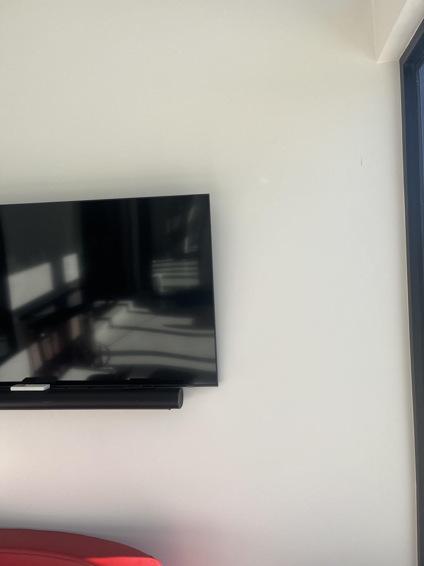 Close-up of a wall-mounted television in a modern living space, showing a clean wall surface near a window.
