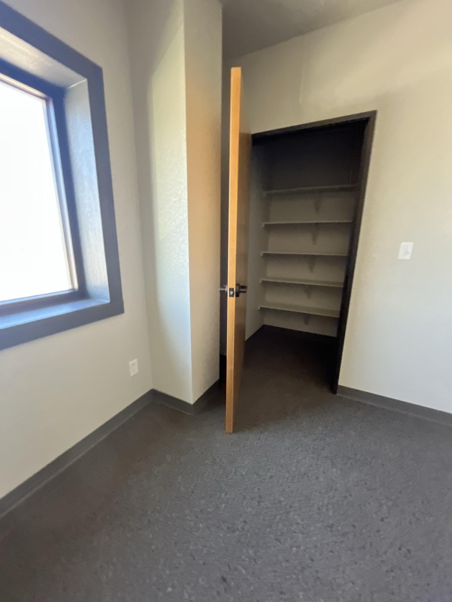 Commercial office room with a window and an open closet with shelves, showcasing clean grey carpet after water damage cleanup.